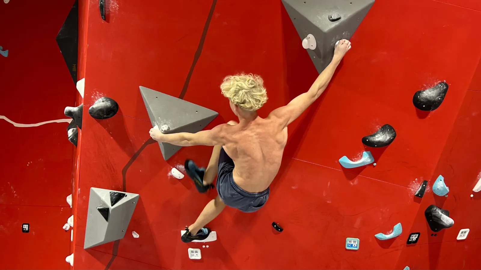 Lezec na červenej boulderingovej stene